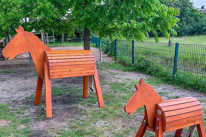 Neue Pferde für die Wilde 13 Zwei Holzpferde für Kinder stehen in einem Garten.